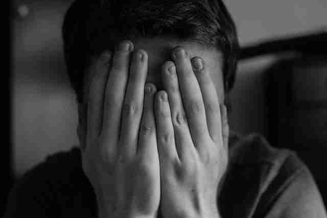 Teen sits with hands covering face in black and white. PDA in teenagers, teen anxiety, and teen depression.