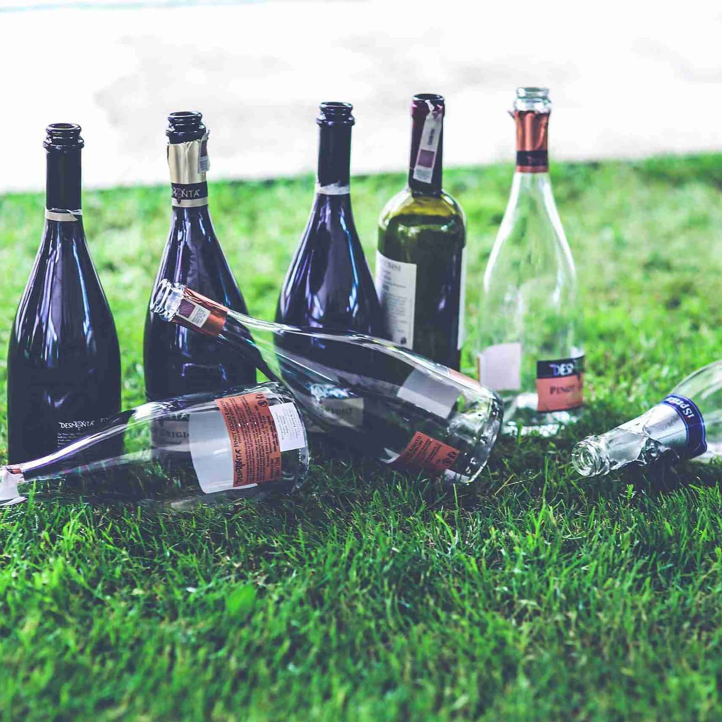 Treating Teen Substance Use - 8 empty glass alcohol bottles sit on the grass.