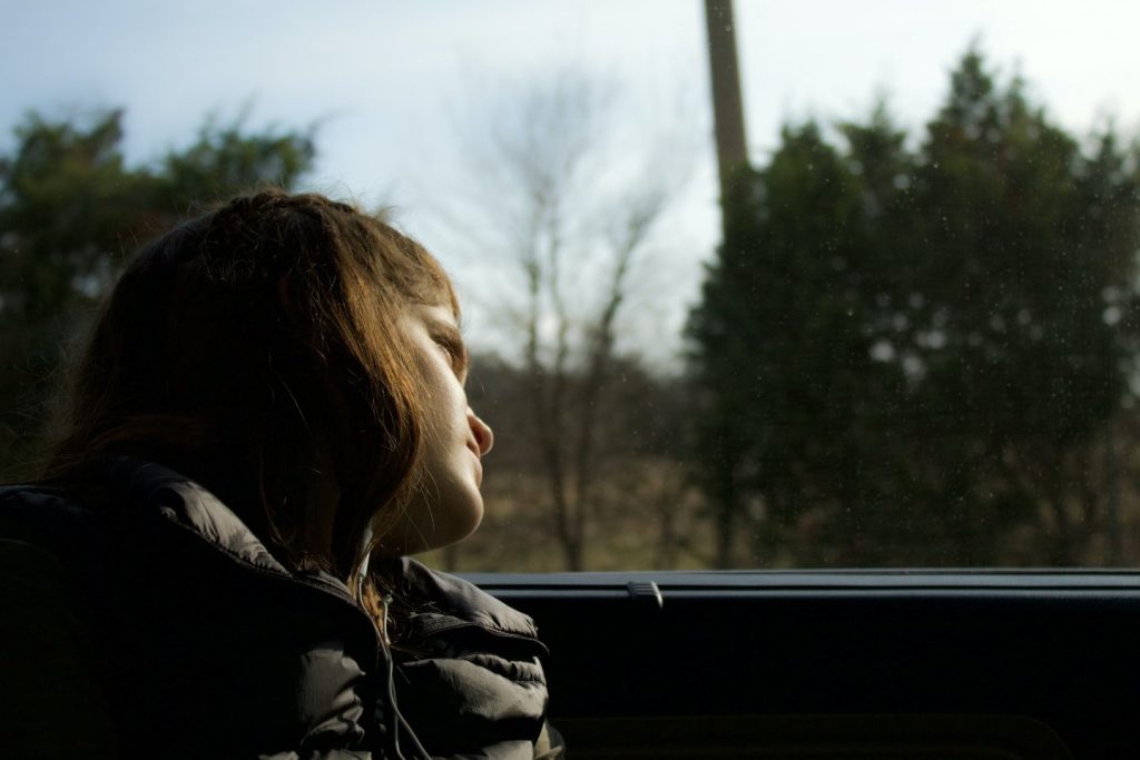 Teen looks out the window of a car with a sad expression on her face.